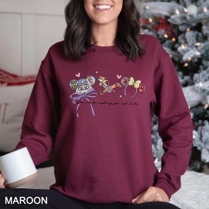 Puede incluir: Sudadera granate con un dise&ntilde;o de personajes de dibujos animados y el texto "You can be anything you wish to be." El dise&ntilde;o incluye un rat&oacute;n con gorra de polic&iacute;a, un zorro y un par de orejas.