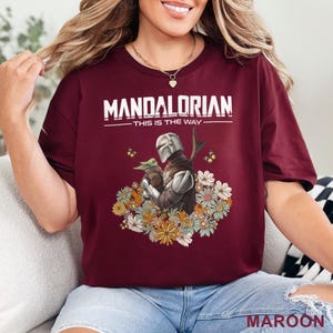 May include: A maroon t-shirt with a white graphic of the Mandalorian and Grogu with the text "Mandalorian - This is the Way" surrounded by flowers.