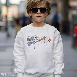 Puede incluir: Sudadera blanca con un gr&aacute;fico de dibujos animados coloridos y el texto "You can be anything you wish to be." El dise&ntilde;o incluye un lazo, corazones y diademas tem&aacute;ticas de personajes. La sudadera la lleva una persona con gafas de sol.