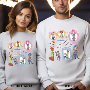 May include: Sport grey and white sweatshirts featuring a colorful Zootopia design. The design includes cartoon characters in frames, hearts, and the text "Welcome to Zootopia". The sweatshirts are displayed on a man and woman.