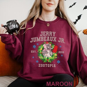 Op de afbeelding: Bordeaux sweatshirt met de tekst "JERRY JUMBEAUX JR." en een cartoon olifant met een kerstmuts en een rood ijsje. De trui heeft ook "EST. 2016" en "ZOOTOPIA".