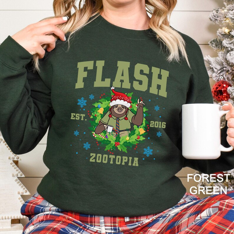 Op de afbeelding: Boszwarte sweatshirt met de tekst "FLASH" en een cartoon luiaard met een kerstmuts. De luiaard staat in een krans met de tekst "EST. 2016 ZOOTOPIA".
