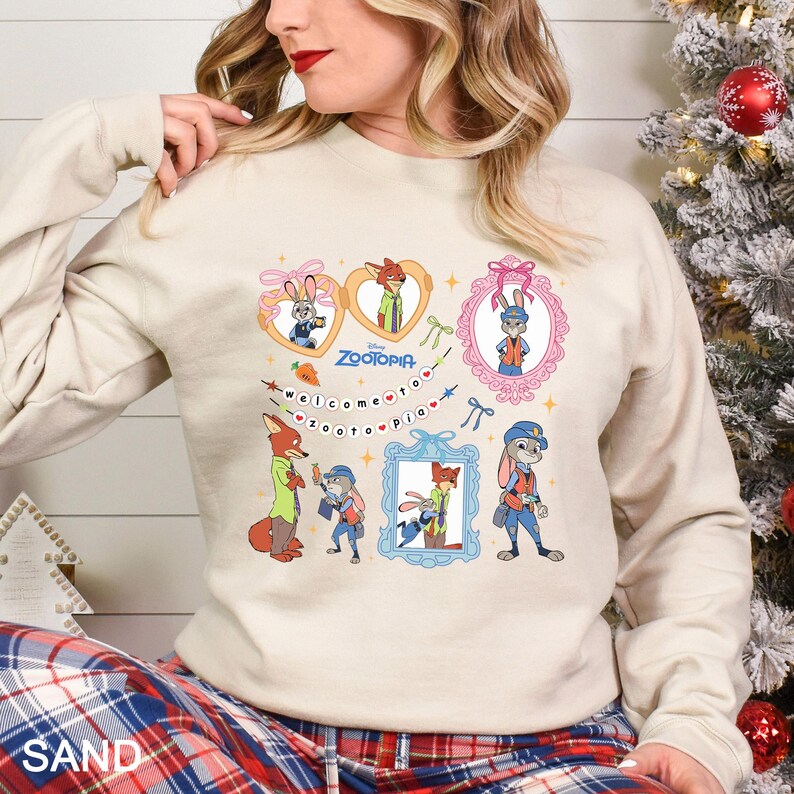 May include: Sand-colored sweatshirt featuring cartoon characters from the movie Zootopia. The design includes images of a fox and a rabbit in various frames, with the text "Welcome to Zootopia" in a playful font.