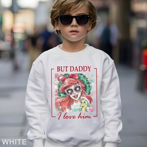 Puede incluir: Sudadera blanca con un gr&aacute;fico de Ariel de La Sirenita con gafas de sol, con el texto "BUT DADDY I love him". El dise&ntilde;o est&aacute; enmarcado en rojo. Sudadera de estilo casual.