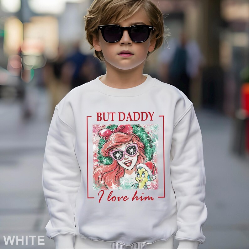 Puede incluir: Sudadera blanca con un gr&aacute;fico de Ariel de La Sirenita con gafas de sol, con el texto "BUT DADDY I love him". El dise&ntilde;o est&aacute; enmarcado en rojo. Sudadera de estilo casual.