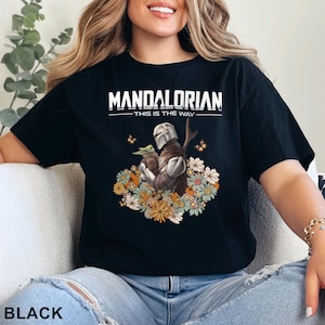 May include: Black t-shirt with a graphic of a Mandalorian character holding a small creature. The text "Mandalorian - This is the Way" is printed on the shirt.