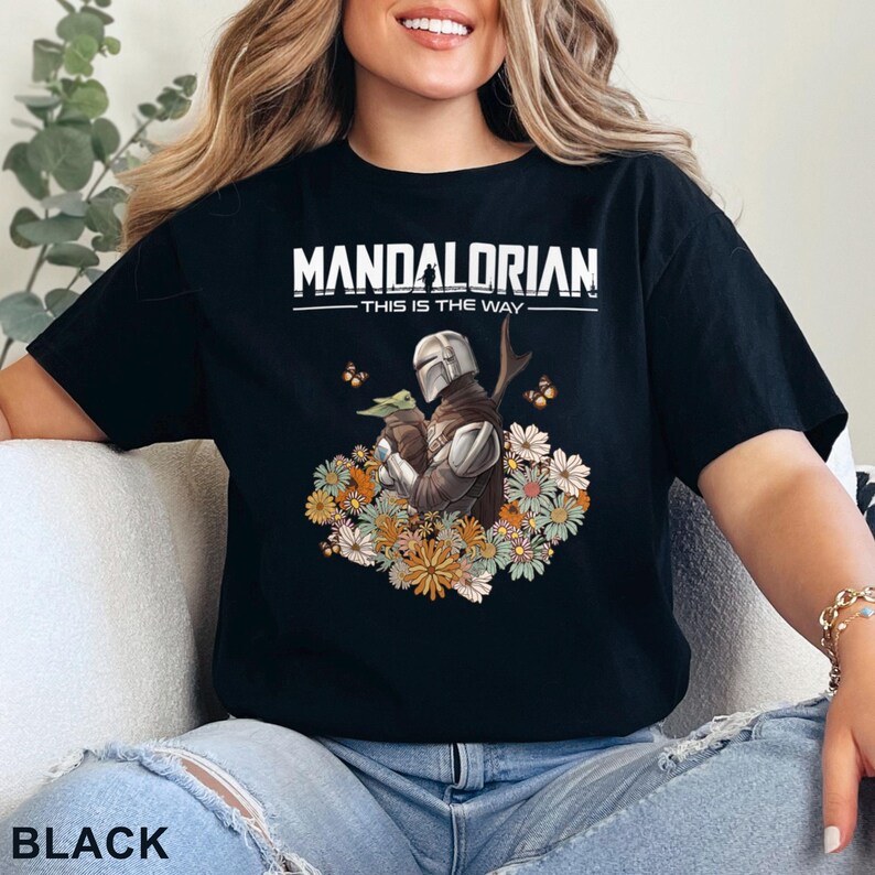 May include: Black t-shirt with a graphic of a Mandalorian character holding a small creature. The text "Mandalorian - This is the Way" is printed on the shirt.