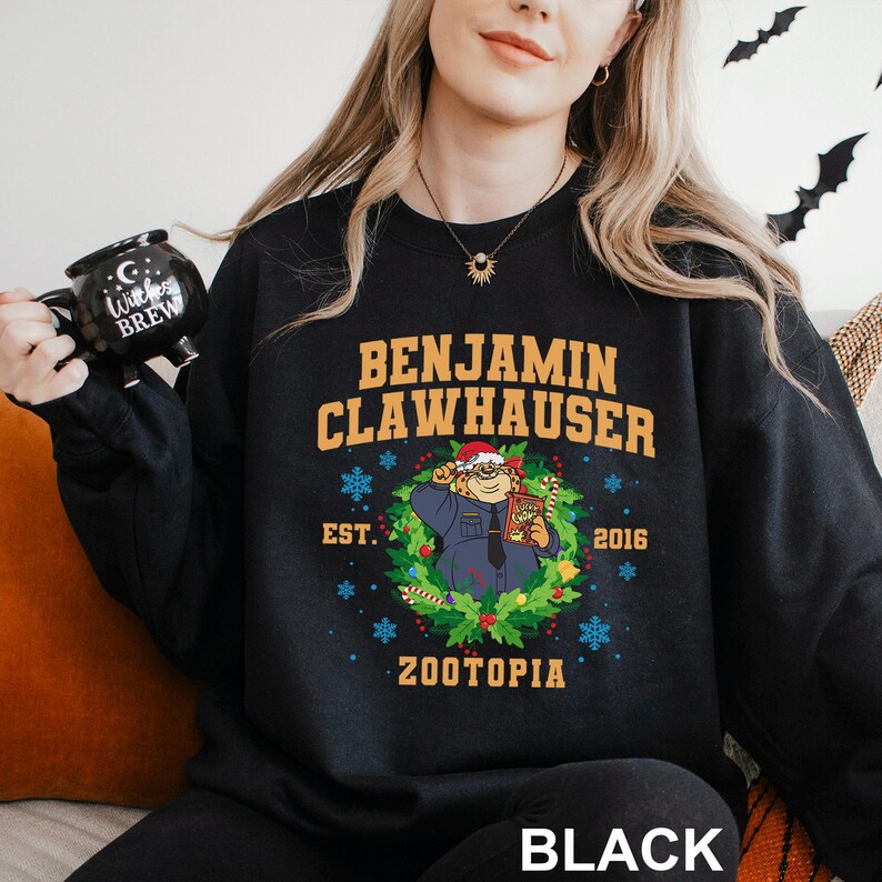 Op de afbeelding: Zwarte sweatshirt met Benjamin Clawhauser uit Zootopia. Het ontwerp bevat de tekst "BENJAMIN CLAWHAUSER" boven een illustratie van het personage in een krans, met "EST. 2016" en "ZOOTOPIA" eronder. Het woord "BLACK" staat onderaan.
