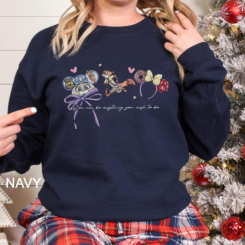 Puede incluir: Sudadera azul marino con personajes de dibujos animados y el texto "You can be anything you wish to be." El dise&ntilde;o incluye un conejo, un zorro y accesorios tem&aacute;ticos. Una cinta morada est&aacute; en la parte inferior del dise&ntilde;o.