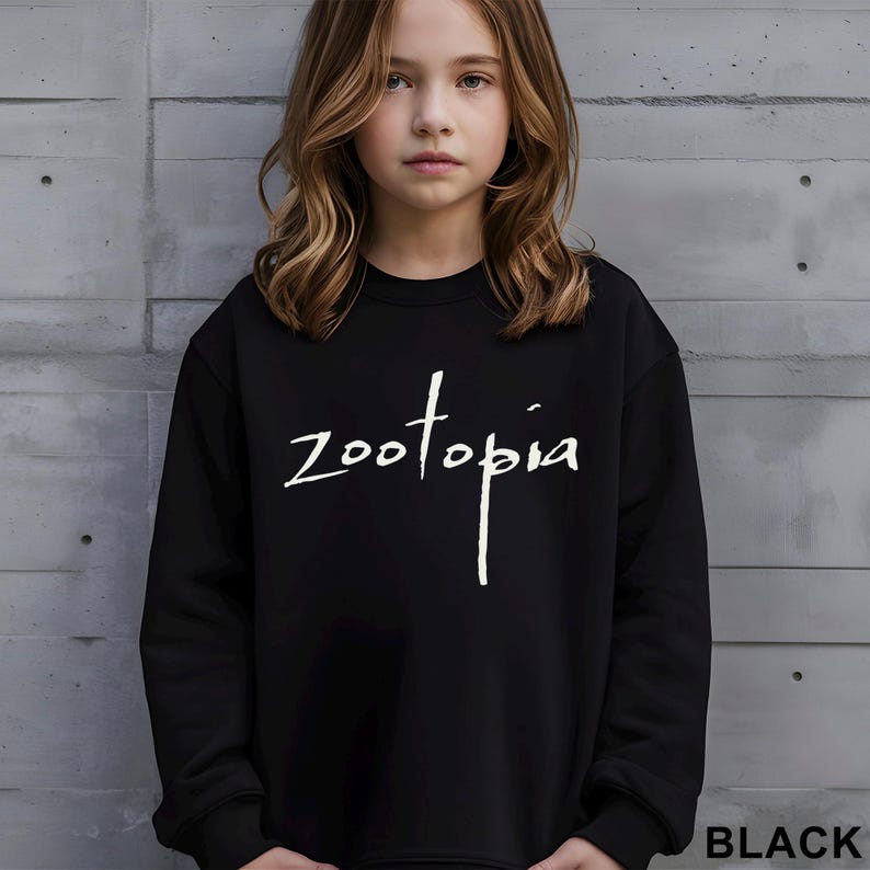 May include: Black crew neck sweatshirt featuring the word "Zootopia" in white script. The sweatshirt is worn by a person. The word "BLACK" is printed in white at the bottom right corner of the image.