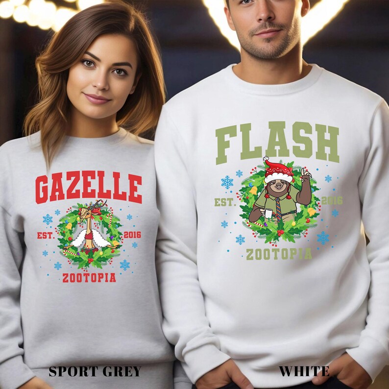 Op de afbeelding: Twee sweatshirts, &eacute;&eacute;n sportgrijs en &eacute;&eacute;n wit, met Zootopia-thema's. Het sportgrijze sweatshirt heeft "GAZELLE" in rood, een cartoon gazelle en de tekst "ZOOTOPIA". Het witte sweatshirt heeft "FLASH" in groen, een luiaard en de tekst "ZOOTOPIA".