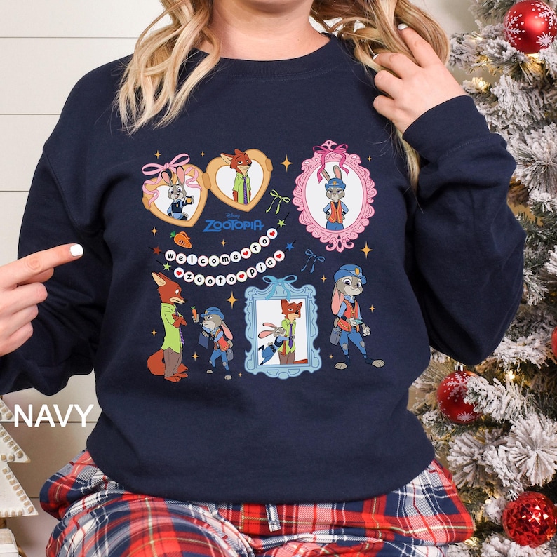 May include: Navy blue sweatshirt featuring Zootopia characters in framed designs. The design includes Judy Hopps and Nick Wilde, with the word "Zootopia" and the word "Welcome" in a circular pattern. The word "NAVY" is printed on the bottom left.
