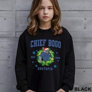 Op de afbeelding: Zwarte sweatshirt met de blauwe tekst "CHIEF BOGO" en een cartoon stier met een kerstmuts en politie-uniform in een krans. Bevat "EST. 2016" en "ZOOTOPIA". Het woord "BLACK" staat rechtsonder.