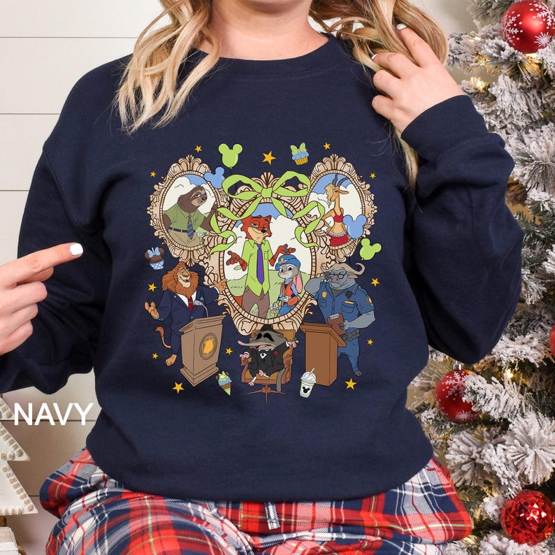 Pode incluir: Camisola azul marinho com uma ilustra&ccedil;&atilde;o de desenho animado colorida de personagens de Zootopia. O design inclui retratos de animais emoldurados, um la&ccedil;o central e detalhes de estrelas. A palavra "NAVY" &eacute; impressa no lado esquerdo da camisola.