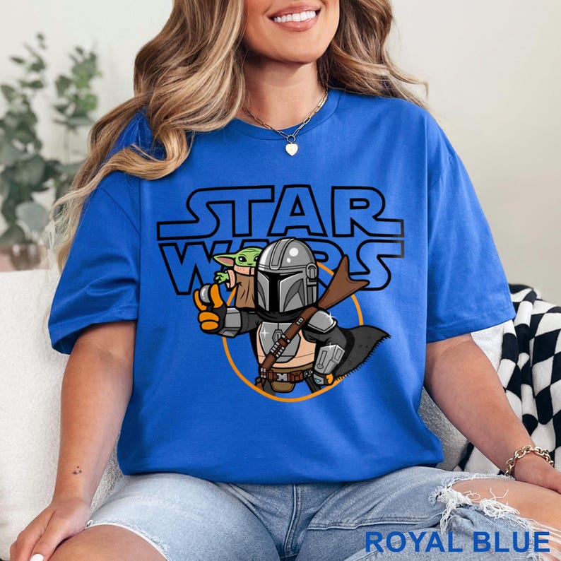 May include: A royal blue t-shirt with a cartoon image of a Mandalorian and Grogu from Star Wars. The text "STAR WARS" is printed in black above the image.
