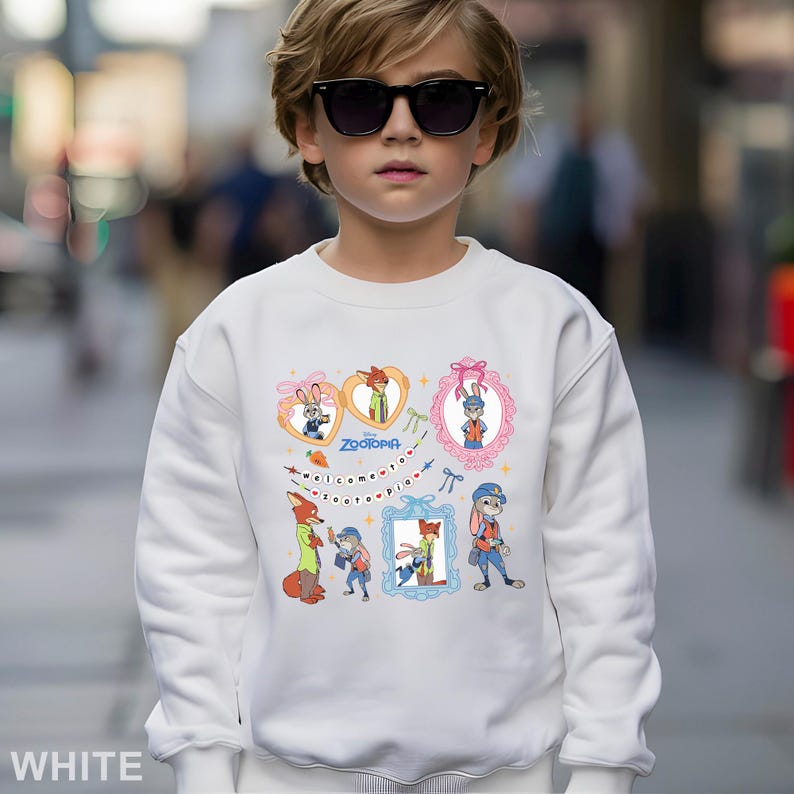 May include: White sweatshirt featuring colorful cartoon characters and the word "Zootopia." The design includes framed images of a rabbit and a fox, with the text "Welcome to Zootopia" below. The sweatshirt is worn by a person wearing sunglasses.