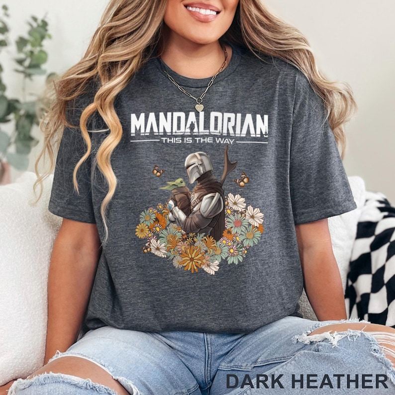 May include: Dark heather grey t-shirt featuring a floral design with The Mandalorian and Grogu. The text "Mandalorian - This is the Way" is printed on the shirt.