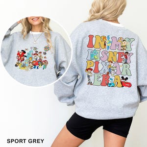 May include: Sport grey sweatshirt featuring a colorful graphic of Disney and Pixar characters on the front and back. The back of the sweatshirt has the text "IN MY DISNEY PIXAR ERA" in a retro font. A fun and comfortable top for Disney fans.