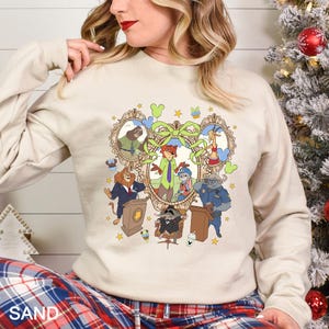 Pode incluir: Um moletom cor de areia com uma ilustra&ccedil;&atilde;o de desenho animado colorida de personagens de um filme de anima&ccedil;&atilde;o popular. O design inclui uma imagem central emoldurada com v&aacute;rios personagens de animais, cercada por estrelas e elementos decorativos.