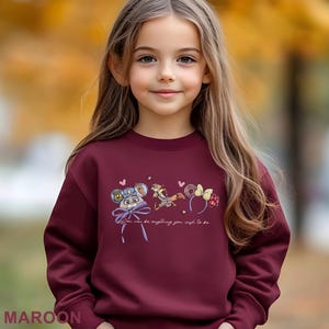 Puede incluir: Sudadera granate con un gr&aacute;fico de personajes de dibujos animados y el texto "You can be anything you wish to be." El dise&ntilde;o incluye un personaje de rat&oacute;n, una ardilla y un lazo. La palabra "MAROON" est&aacute; impresa en la parte inferior.