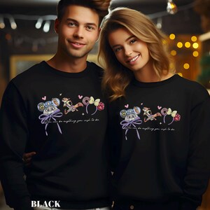 Puede incluir: Sudaderas negras con un dise&ntilde;o de dibujos animados que presenta un rat&oacute;n, una ardilla listada y otros elementos. El dise&ntilde;o incluye el texto "You can be anything you wish to be." Llevadas por un hombre y una mujer.