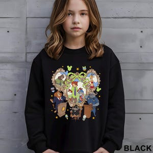 Pode incluir: Camisola preta com um gr&aacute;fico de desenho animado colorido de personagens de animais em molduras ornamentadas. O design inclui um arranjo central em forma de cora&ccedil;&atilde;o com um la&ccedil;o verde e v&aacute;rios personagens. A palavra "BLACK" est&aacute; impressa no canto inferior direito.