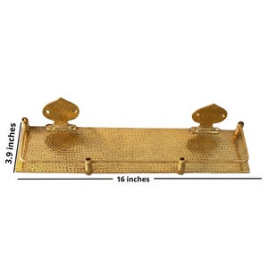 Hammered brass shelf installed in a bathroom, neatly organizing perfume bottles, a small plant, and rolled hand towels. The gold brass contrasts beautifully against the wall.