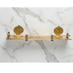 Front view of a handmade hammered brass floating shelf mounted on a wall. The shelf features a shiny, unlacquered gold finish and a front lip to keep items secure.