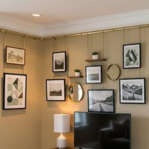 Pode incluir: Uma parede de galeria com arte emoldurada, espelhos e pequenas prateleiras. As molduras são pretas e a arte inclui desenhos geométricos, paisagens e imagens abstratas. A decoração da parede é suspensa por uma barra dourada.