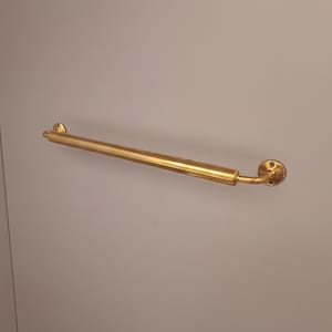 Könnte beinhalten: Ein goldfarbener, gerader Haltegriff mit abgerundeten Enden und einer kreisförmigen Montageplatte. Die Stange ist auf einer hellgrauen Oberfläche montiert und bietet Halt und Sicherheit.