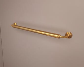 May include: A gold-colored, straight grab bar with rounded ends and a circular mounting plate. The bar is mounted on a light gray surface, providing support and safety in bathrooms or other areas.