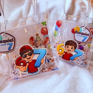 May include: Two clear plastic party favor bags with handles. Each bag features a cartoon illustration of a boy holding the number 6 or 7, with the text "Ezequiel is now 7". The bags are decorated with balloons and a mouse wearing a party hat.