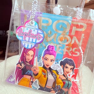 May include: Clear plastic party favor bag with a colorful design. The bag features a graphic of three animated women and the text "POP MONSTERS". A tag reads "Sophia's Birthday Party".