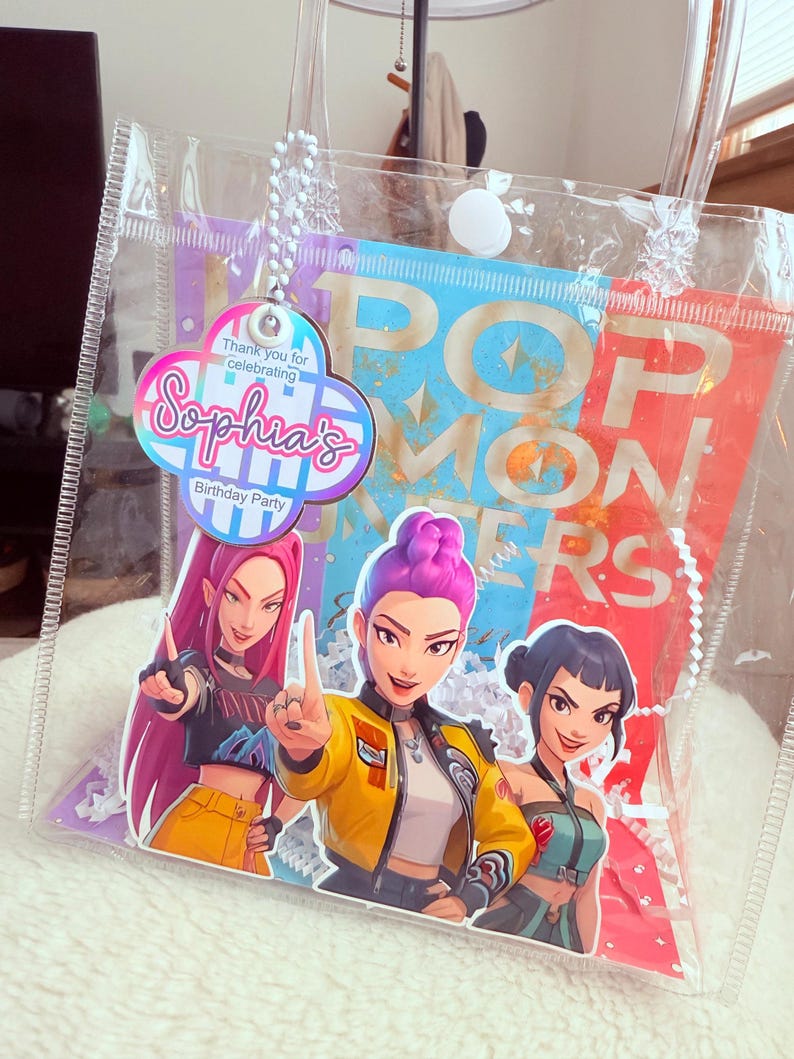 May include: Clear plastic party favor bag with a colorful design. The bag features a graphic of three animated women and the text "POP MONSTERS". A tag reads "Sophia's Birthday Party".