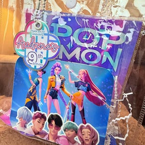 Puede incluir: Decoraci&oacute;n de fiesta de cumplea&ntilde;os con un gr&aacute;fico colorido de personajes animados. El dise&ntilde;o incluye el texto "Audrina's 9th Birthday" y "POP MON". La decoraci&oacute;n est&aacute; dentro de una bolsa de pl&aacute;stico transparente.