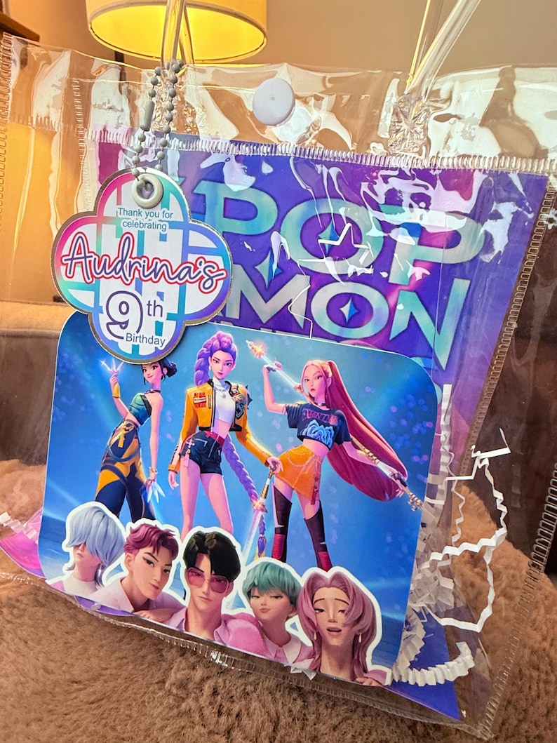 Puede incluir: Decoraci&oacute;n de fiesta de cumplea&ntilde;os con un gr&aacute;fico colorido de personajes animados. El dise&ntilde;o incluye el texto "Audrina's 9th Birthday" y "POP MON". La decoraci&oacute;n est&aacute; dentro de una bolsa de pl&aacute;stico transparente.
