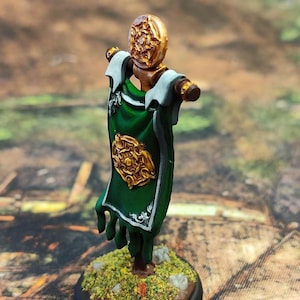 May include: A miniature green banner with a gold emblem and white trim, mounted on a wooden pole and base. The banner is decorated with a stylized floral design.