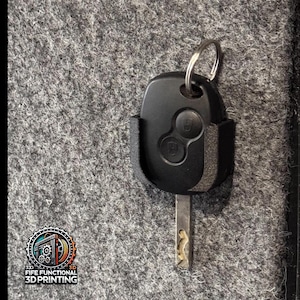 May include: A black car key with a key fob holder. The key has two buttons and a metal key blade. The key is in a black holder. The logo for Fife Functional 3D Printing is in the lower left corner.