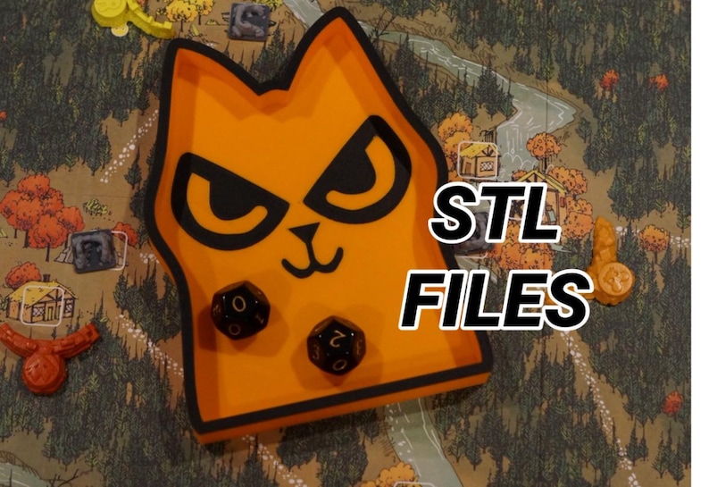 May include: An orange cat-shaped dice tray with black accents and two dice inside. The tray has the text "STL FILES" in white. The background shows a game board with miniature game pieces.
