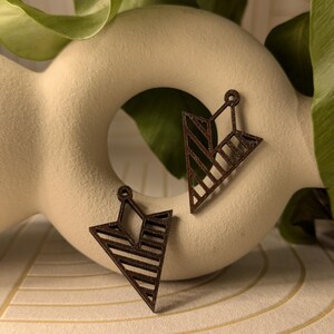 May include: Two brown wooden geometric triangle earrings with a striped pattern.