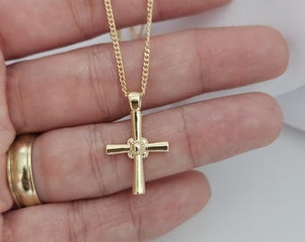 Könnte beinhalten: Eine goldene Kettenkette mit einem kleinen goldenen Kreuzanhänger. Das Kreuz hat ein strukturiertes Design und einen kleinen Kreis in der Mitte.