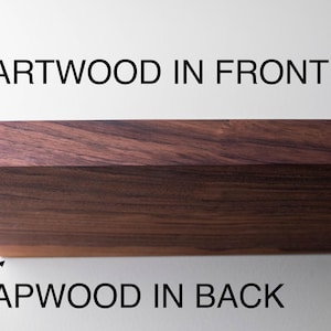 May include: Close-up of a section of hardwood, showcasing the grain and color variations. The text indicates "HEARTWOOD IN FRONT" and "SAPWOOD IN BACK", highlighting the wood's natural features. The wood has a rich, dark brown hue.