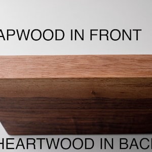 May include: Close-up of a wooden board with two distinct sections. The top section, labeled "SAPWOOD IN FRONT," is a lighter brown, while the lower section, labeled "HEARTWOOD IN BACK," is a darker brown. The board's edge is angled.