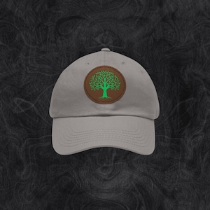 Könnte beinhalten: Eine graue Baseballkappe mit einem braunen Lederpatch, der ein grünes Baumdesign zeigt.