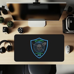 Peut inclure: Tapis de bureau rectangulaire noir avec le logo "DEV CORPS" bleu et blanc, représentant un crâne et des outils croisés. Le tapis comprend également le texte "Astroforma Design AD". Un écran d'ordinateur, une souris et un casque sont visibles.