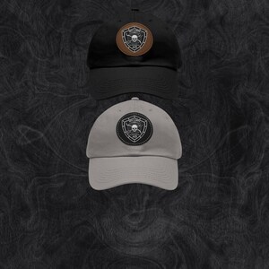 Puede incluir: Dos gorras de béisbol, una negra y otra gris, con un parche de calavera y huesos cruzados en la parte delantera. El parche es de cuero marrón con costuras blancas y el texto "SKY CORP" sobre la calavera.