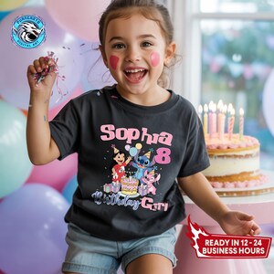 Puede incluir: Una ni&ntilde;a sonr&iacute;e, vistiendo una camiseta gris oscuro con el nombre "Sophia" y el n&uacute;mero "8" en rosa. La camiseta presenta un gr&aacute;fico de dibujos animados de personajes y las palabras "Birthday Girl". Una tarta de cumplea&ntilde;os con velas encendidas est&aacute; en el fondo.