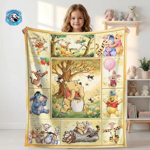 May include: A yellow blanket featuring illustrations of Winnie the Pooh and friends, including Piglet, Tigger, and Eeyore. The blanket has a personalized name in the center and a gold border. The blanket is suitable for a child.