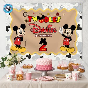 May include: A rectangular birthday party backdrop featuring a tan center with a scalloped gold border, displaying the text "Oh Twodles Daniel is turning 2" alongside two Mickey Mouse illustrations, set against a white background with gray mouse ears.
