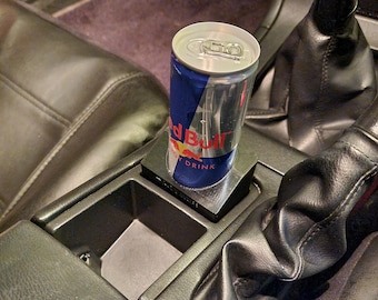 May include: A black 3D printed cup holder for a car, with a red bull energy drink can inside.